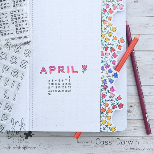Calendar page for April with decorative elements and a pen on a wooden surface.