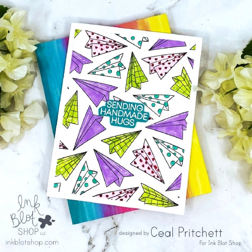 Colorful card with paper airplane pattern and 'Sending Handmade Hugs' text on a marble surface with flowers.